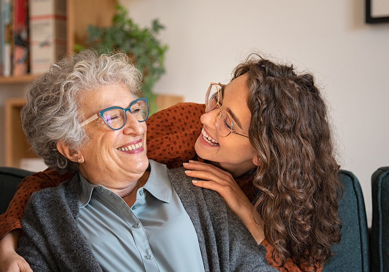 Old grandmother and adult granddaughter hugging at home and look MEDICARE PART D HELP